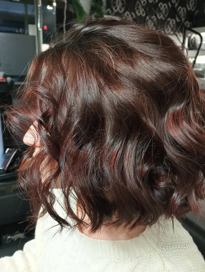 Corte de pelo corto, ondulado y castaño rojizo con rizos en capas, visto de perfil.