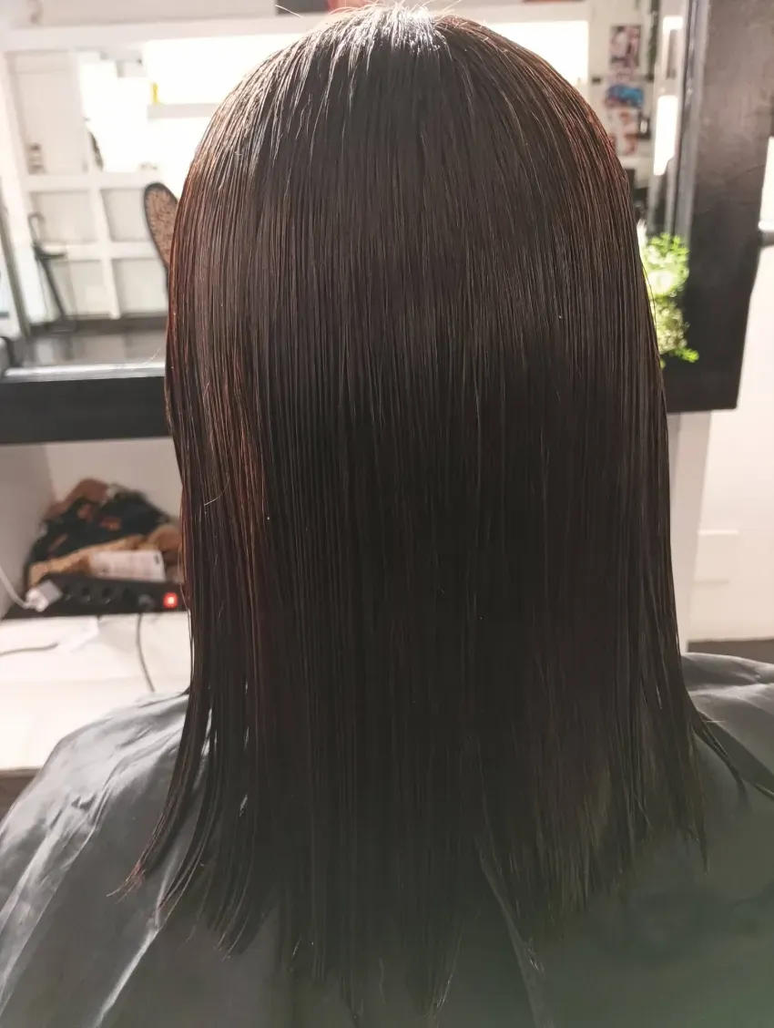 Vista posterior de cabello negro liso y mojado en una silla de peluquería.