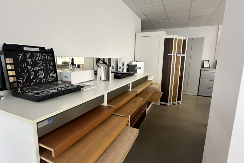 Innenansicht eines Ausstellungsraums für Bodenbeläge mit Holzmustern auf einem Regal und verschiedenen Zierleisten.