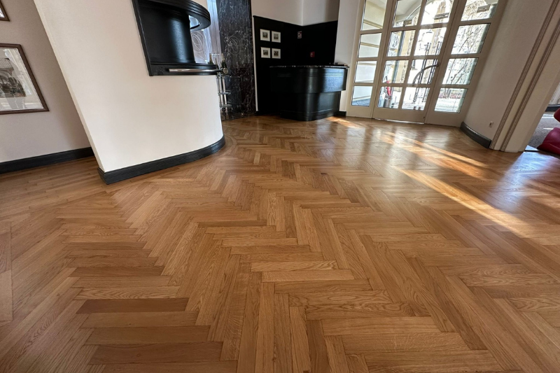 Fischgrätparkett in einem Raum mit einer gebogenen Wand und einem schwarzen Schrank.