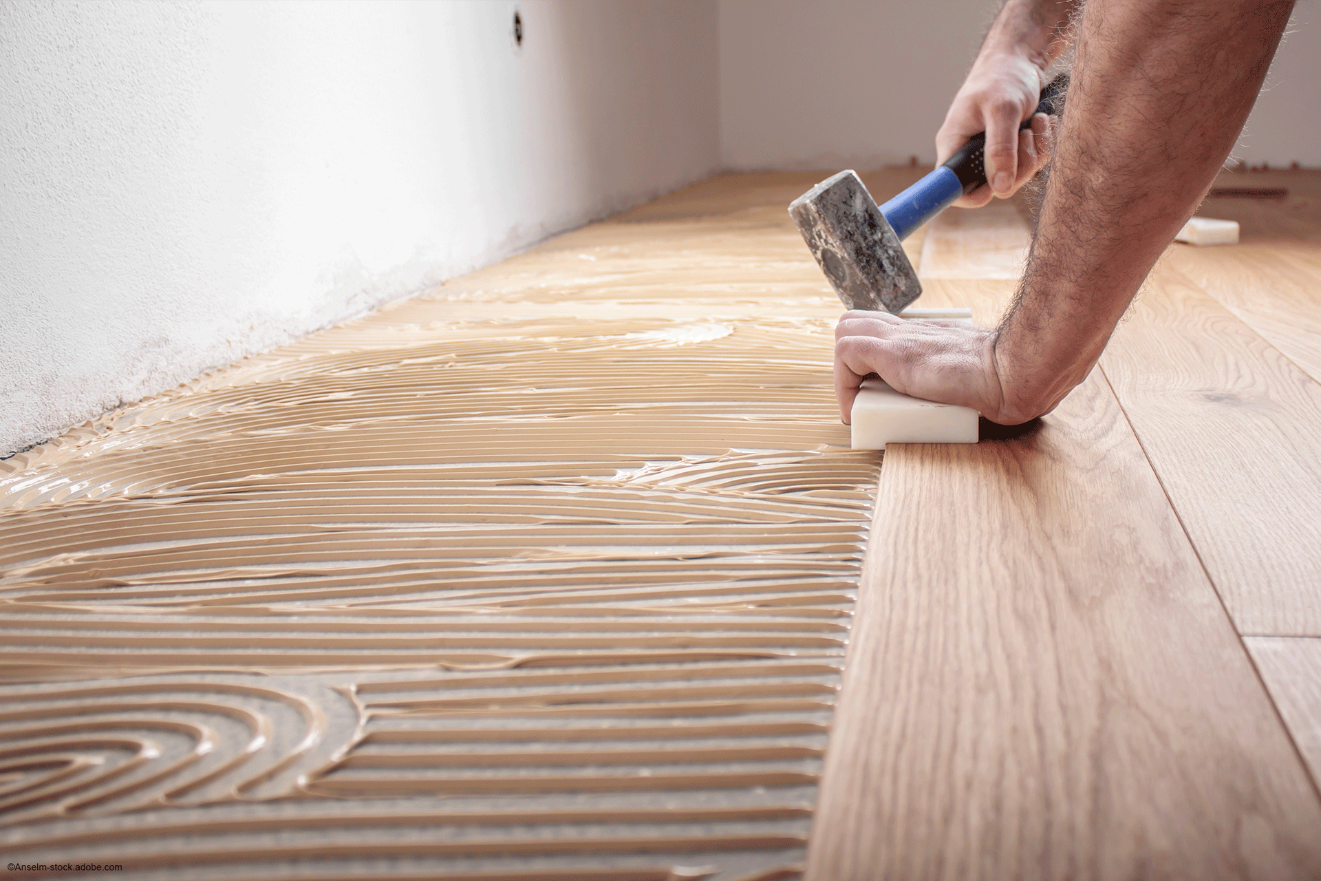 Eine Person befestigt in einem Raum Holzdielen mit einem Gummihammer.