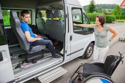 Eine Frau mit einem Koffer steigt auf einem Parkplatz in ein Auto. Mietwagen Gemünden