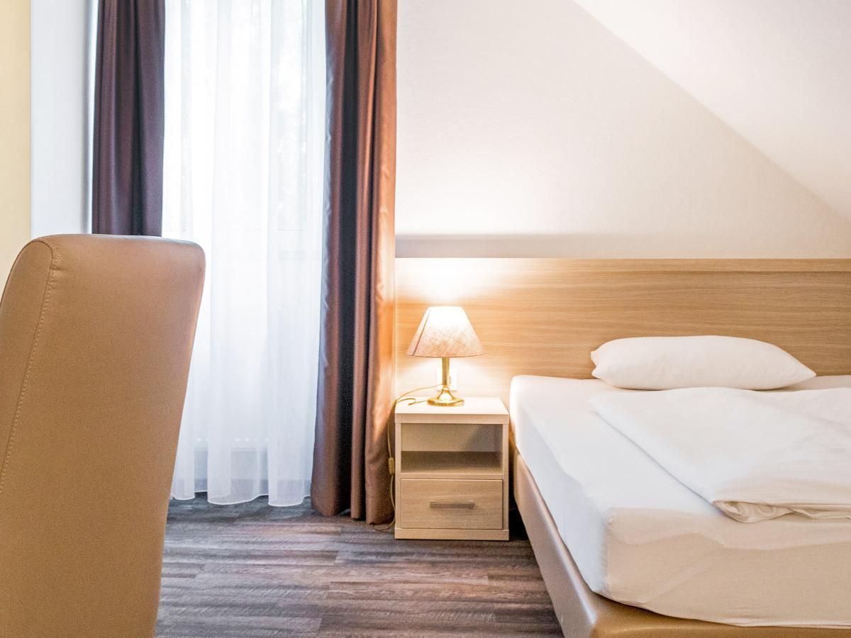 Ein Hotelzimmer mit Bett, Nachttisch, Lampe und Stuhl.