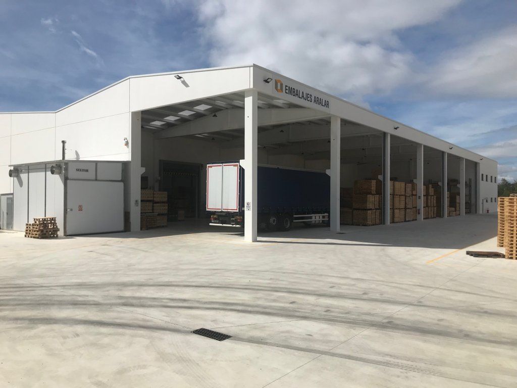 Almacén blanco con bahías abiertas, muelles de carga y un camión.