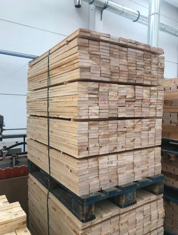 Pila de madera de color claro sobre paletas en un entorno industrial, sujeta con correas negras.