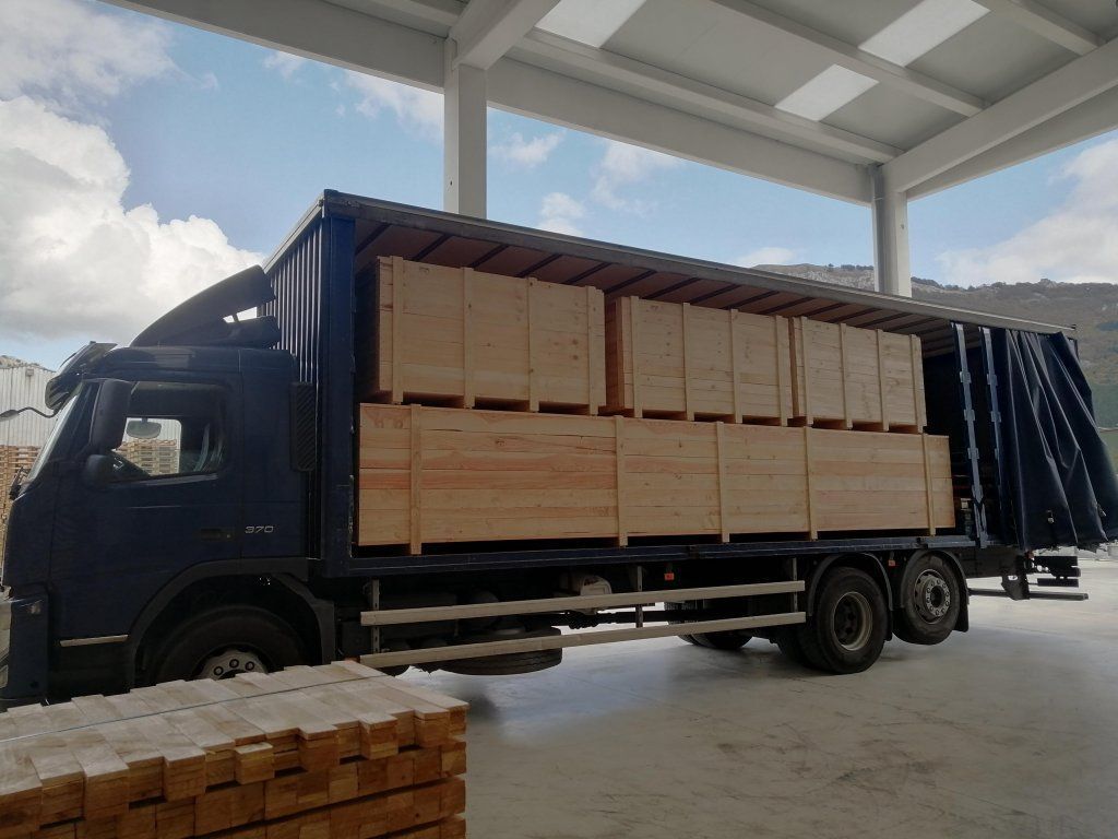 Camión cargado con cajas de madera en un almacén, bajo un techo blanco.