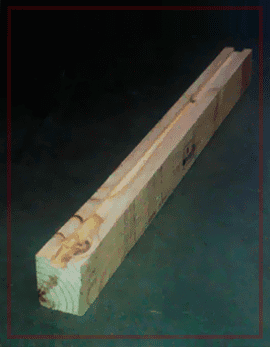 Viga rectangular de madera con un lado ranurado sobre una superficie oscura.