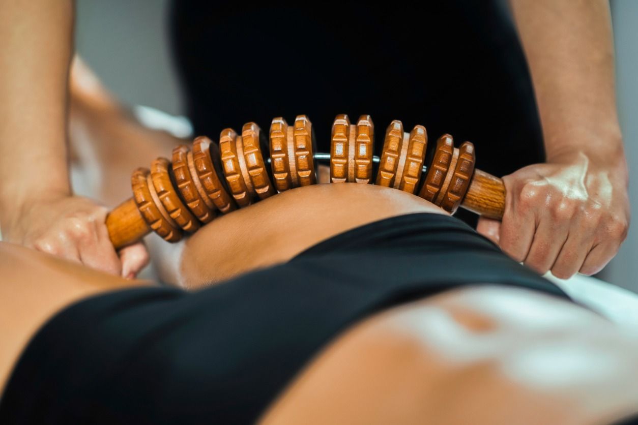 Terapeuta que utiliza una herramienta de masaje de madera en la espalda baja de una persona.