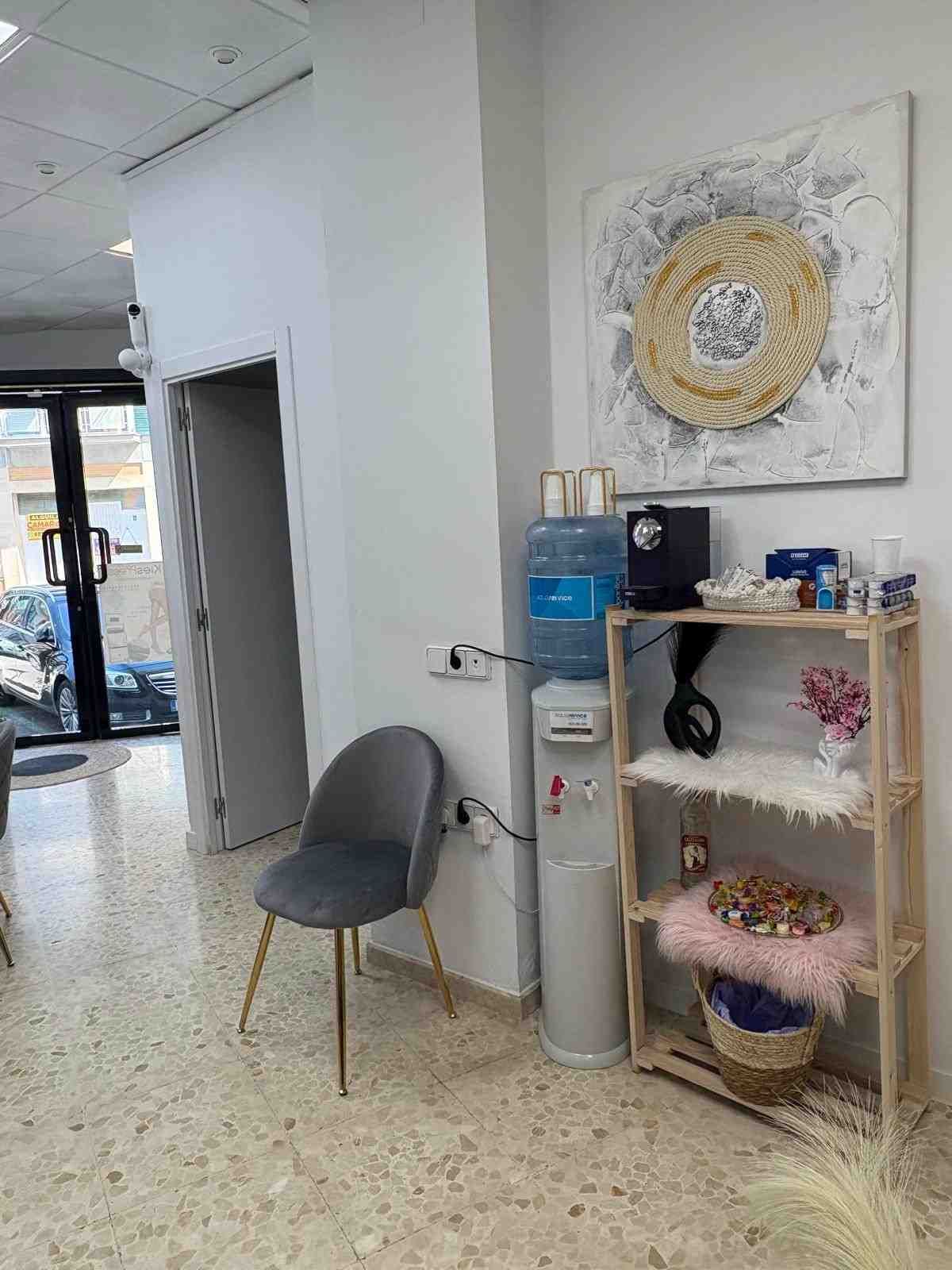 En una habitación bien iluminada, una silla gris se encuentra junto a un dispensador de agua.