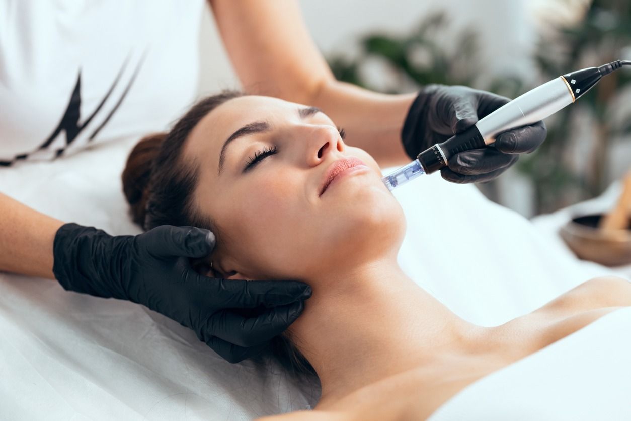 Mujer recibiendo un tratamiento facial con microagujas; manos en guantes negros, iluminación suave.