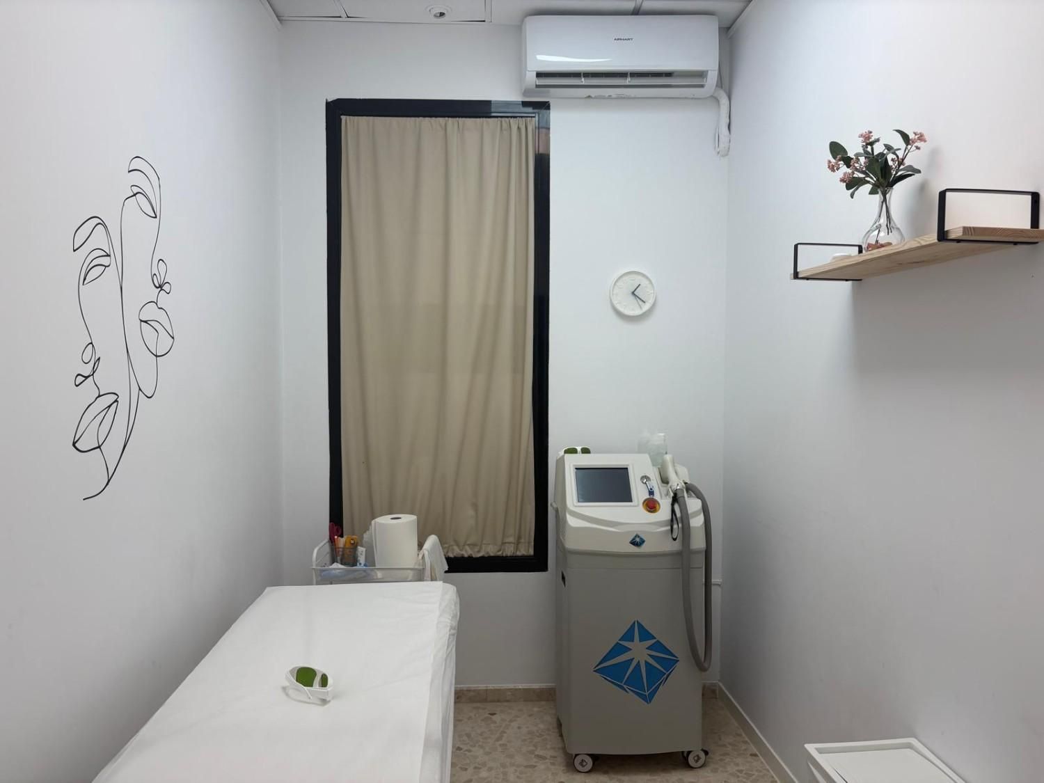 Una sala de tratamiento limpia con una camilla de masaje blanca, una máquina láser.