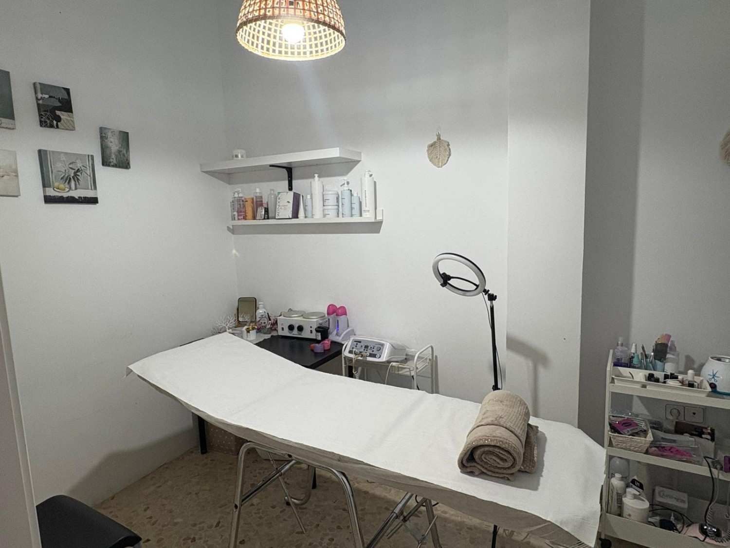 Una sala de tratamiento bien iluminada que cuenta con una camilla de masaje blanca con una toalla enrollada, un aro de luz.