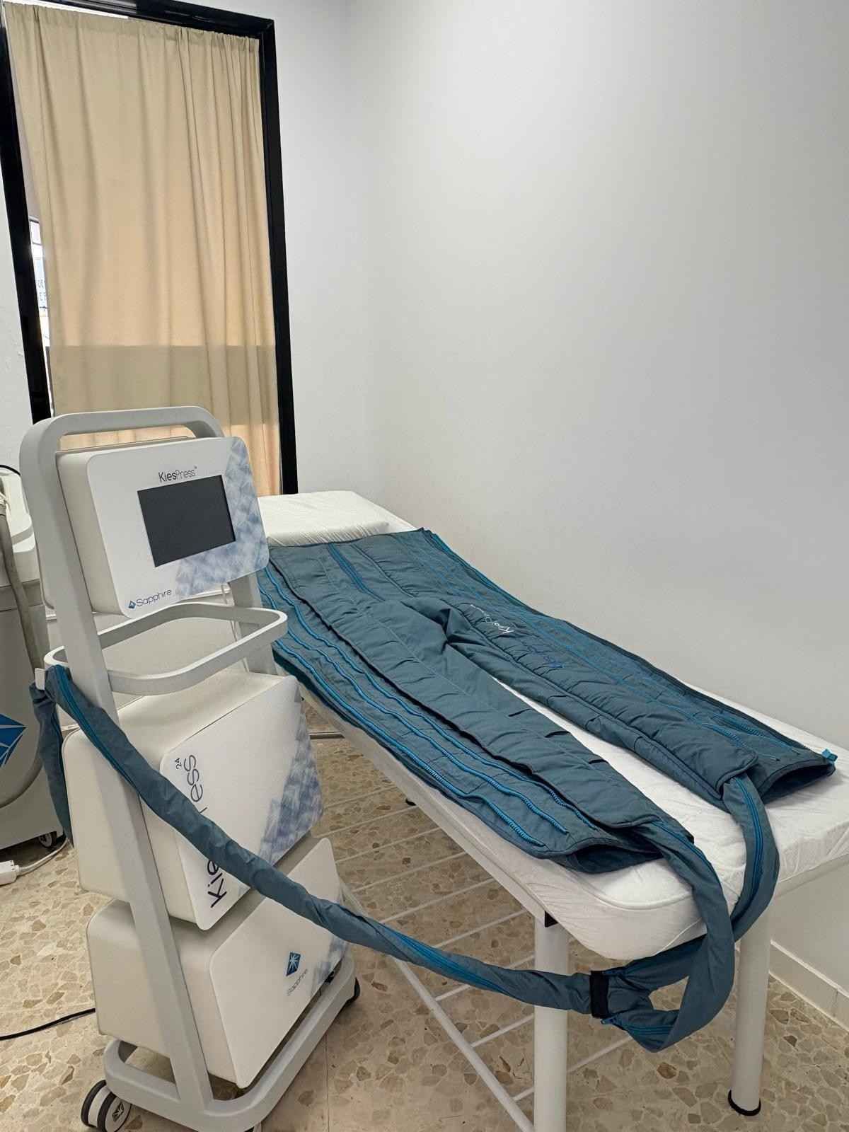 Una máquina de presoterapia médica con mangas inflables azules para las piernas, dispuesta sobre una camilla.