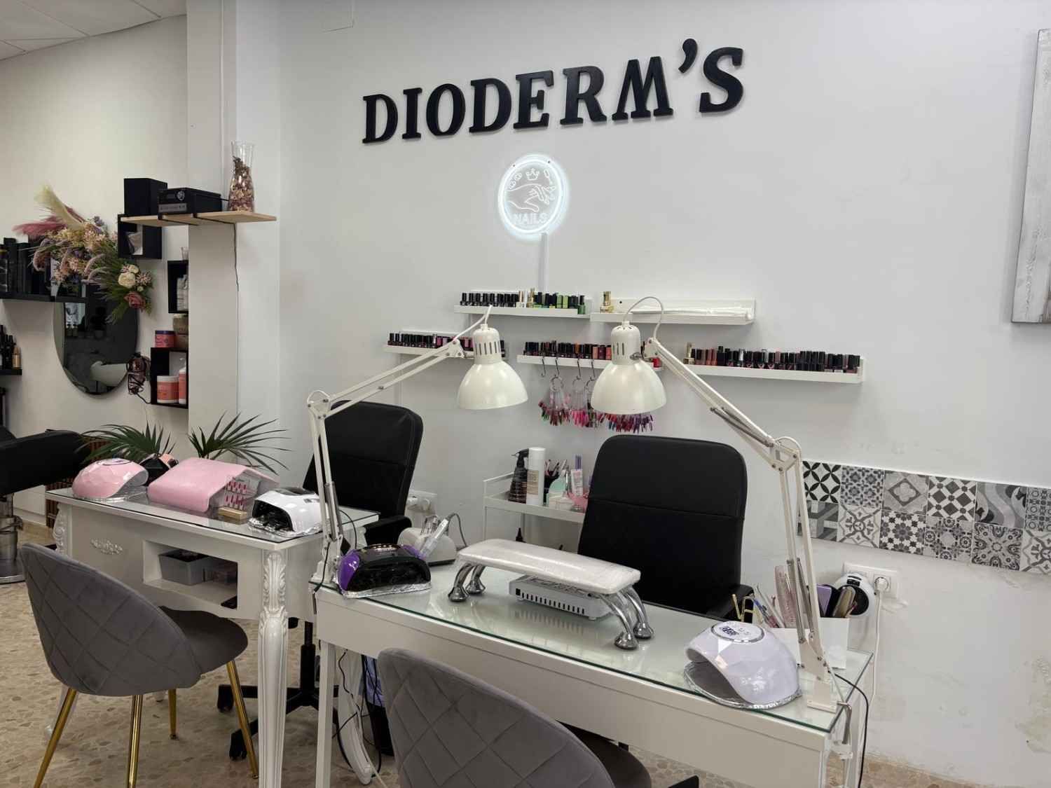 Interior de un salón de manicura con dos mesas blancas para manicura, sillas grises a juego.