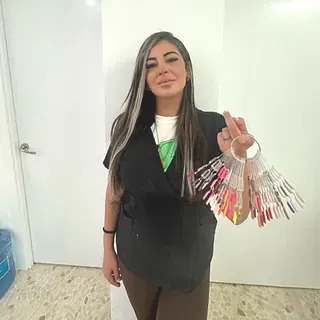 Mujer sosteniendo muestras de color de esmalte de uñas, de pie en el interior cerca de una pared blanca.