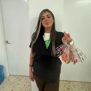 Mujer sosteniendo muestras de color de esmalte de uñas, de pie en el interior cerca de una pared blanca.