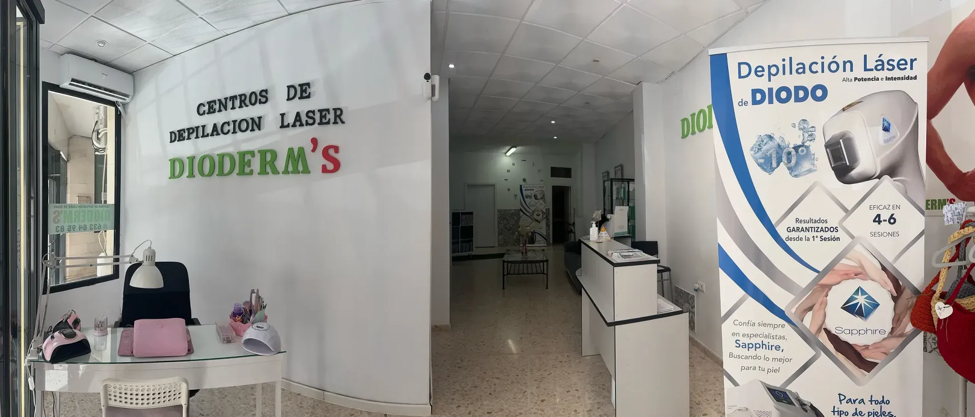Interior de una clínica de depilación láser, DIODERM'S. Paredes blancas, recepción y carteles promocionales.
