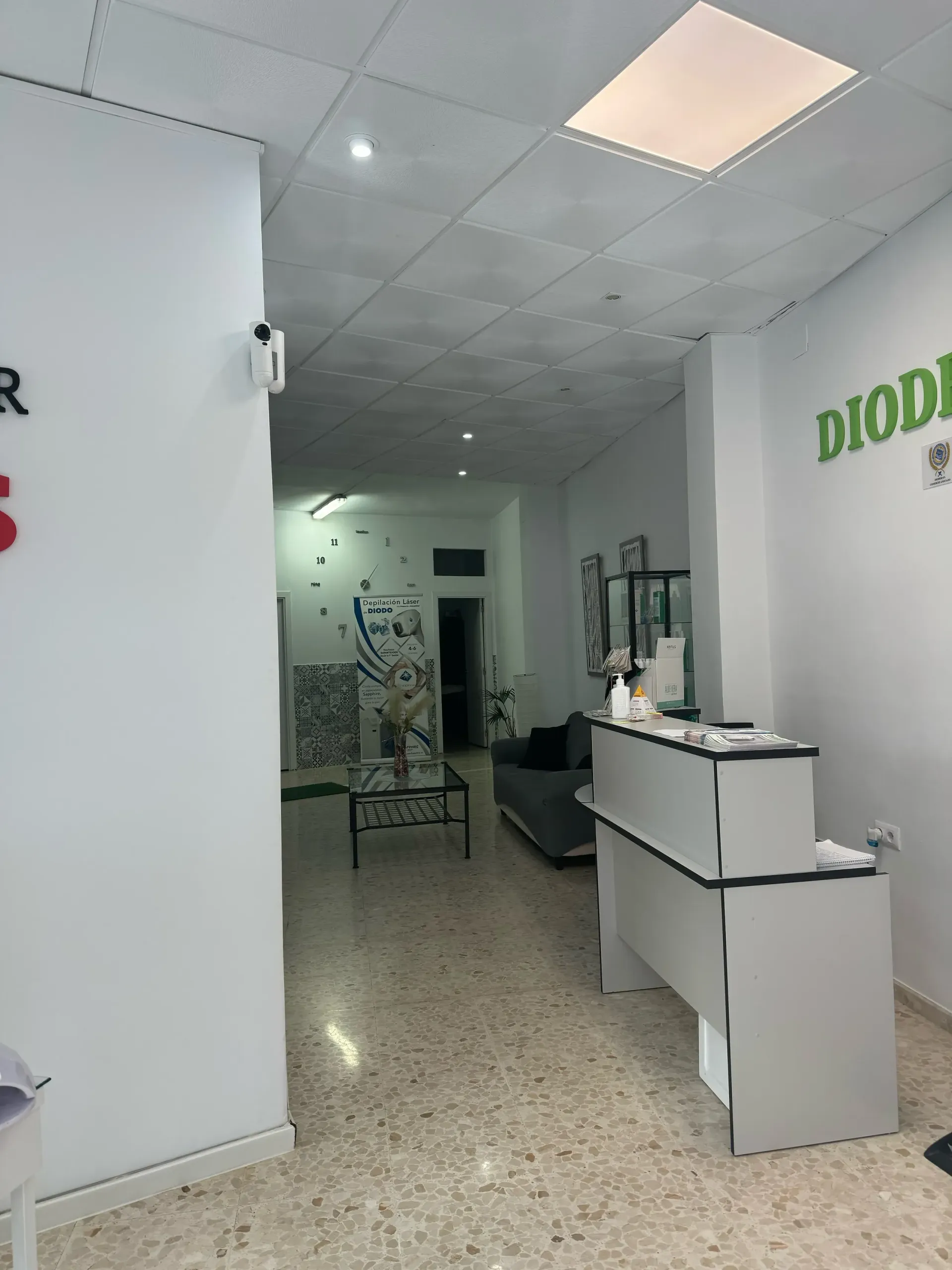 Un área de recepción estrecha y luminosa con un escritorio blanco y una zona de espera visible a la distancia.