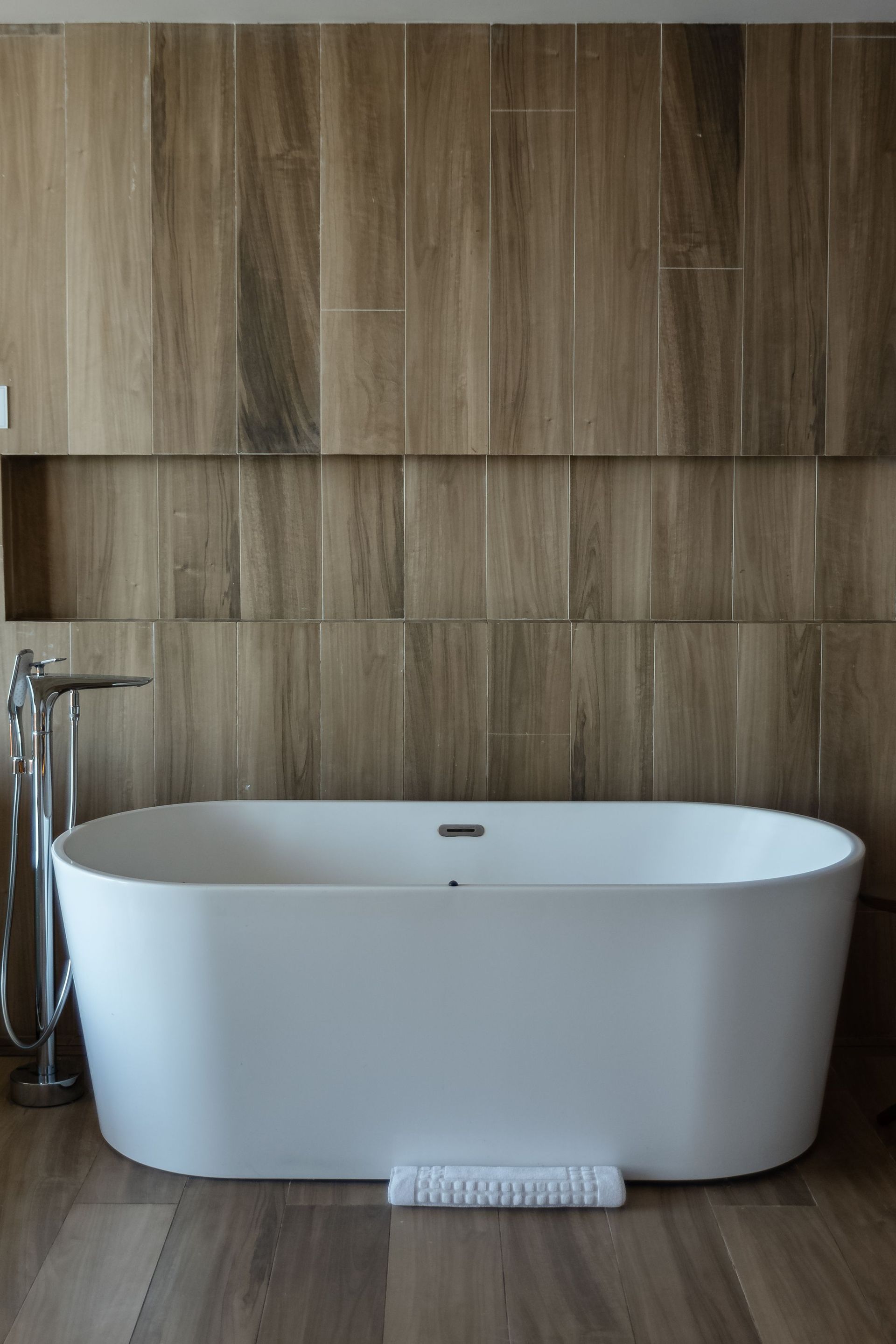 Freistehende weiße Badewanne vor einer holzvertäfelten Wand in einem modernen Badezimmer