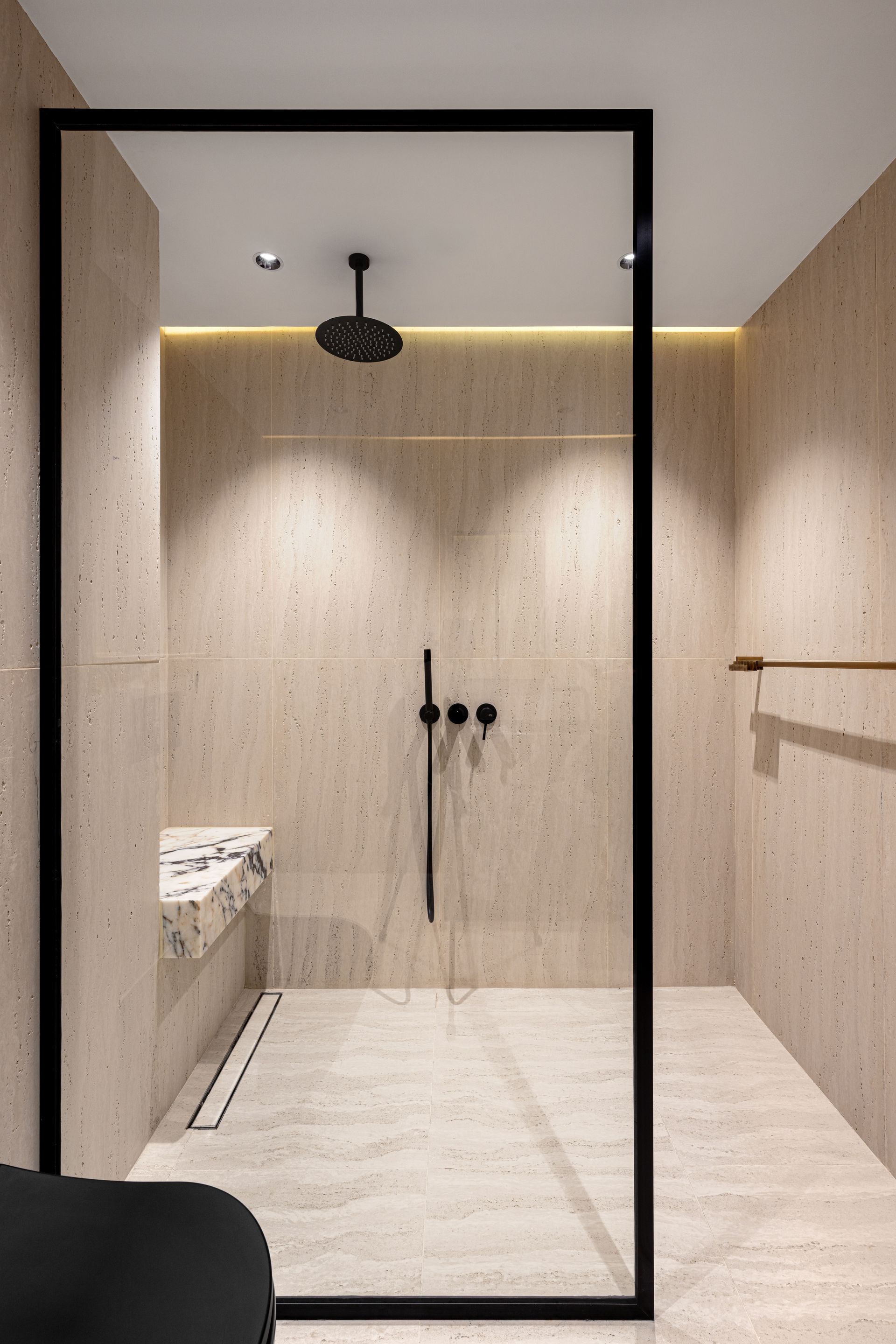 Modernes, minimalistisches Badezimmer mit beigen Steinwänden, bodengleicher Dusche, schwarzem Rahmen und Regenduschkopf