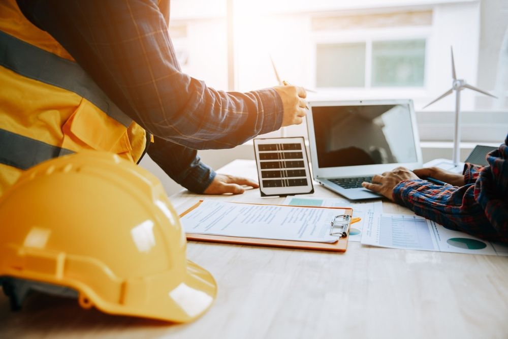 Los ingenieros revisan los planes de energía renovable: paneles solares, modelos de turbinas eólicas, computadora portátil