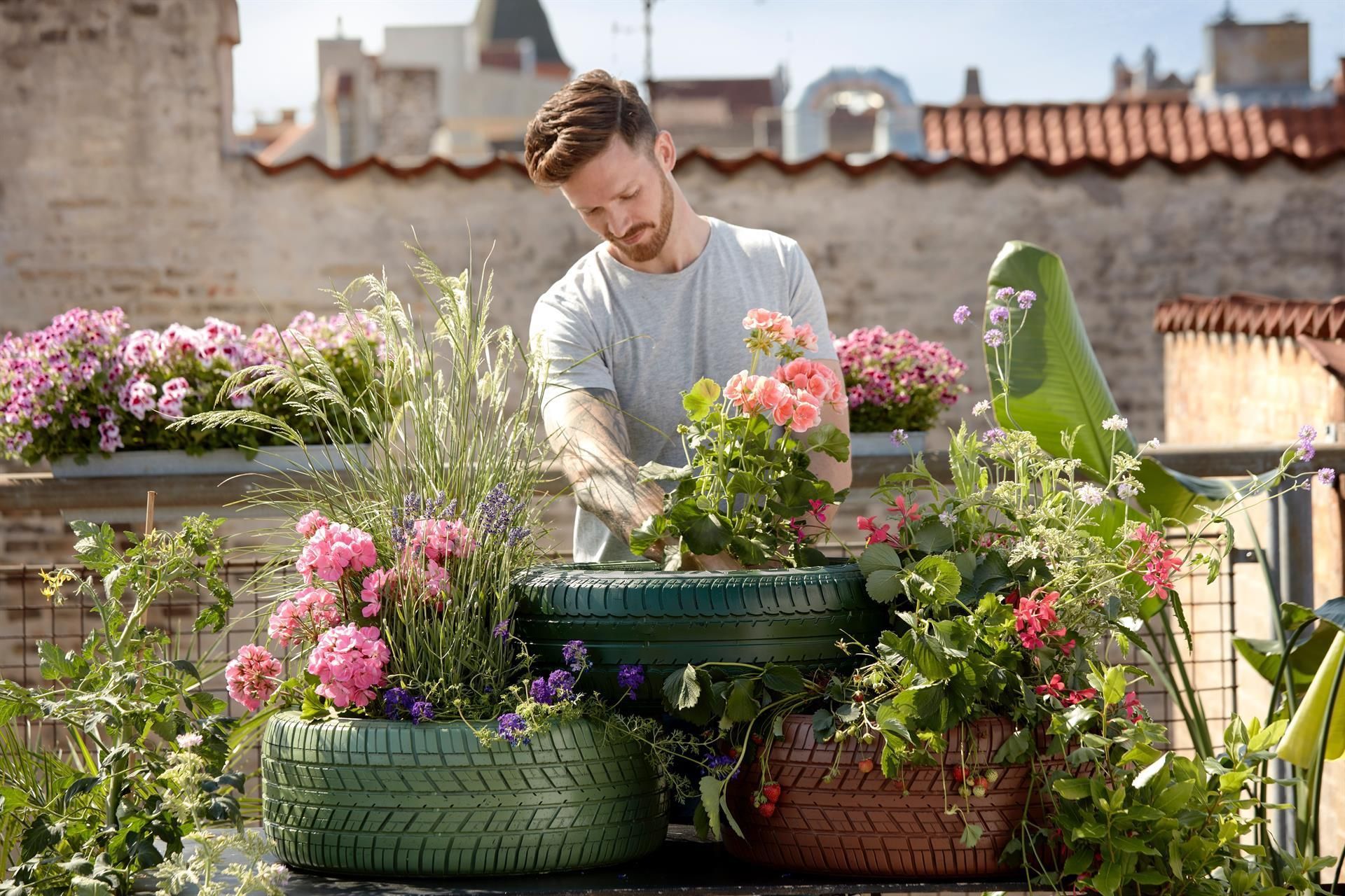 Ein Mann pflanzt Blumen in einen Reifenkübel auf einem Balkon.