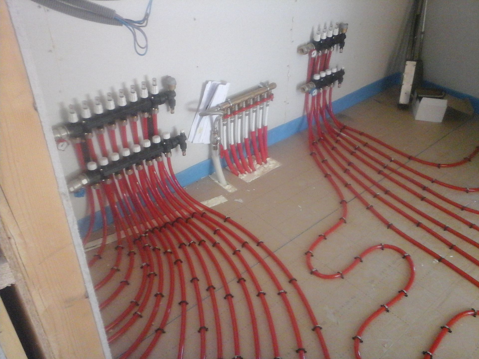 Collecteurs de chauffage pour sol radiant avec plusieurs tuyaux rouges raccordés, installés sur un mur intérieur non fini.