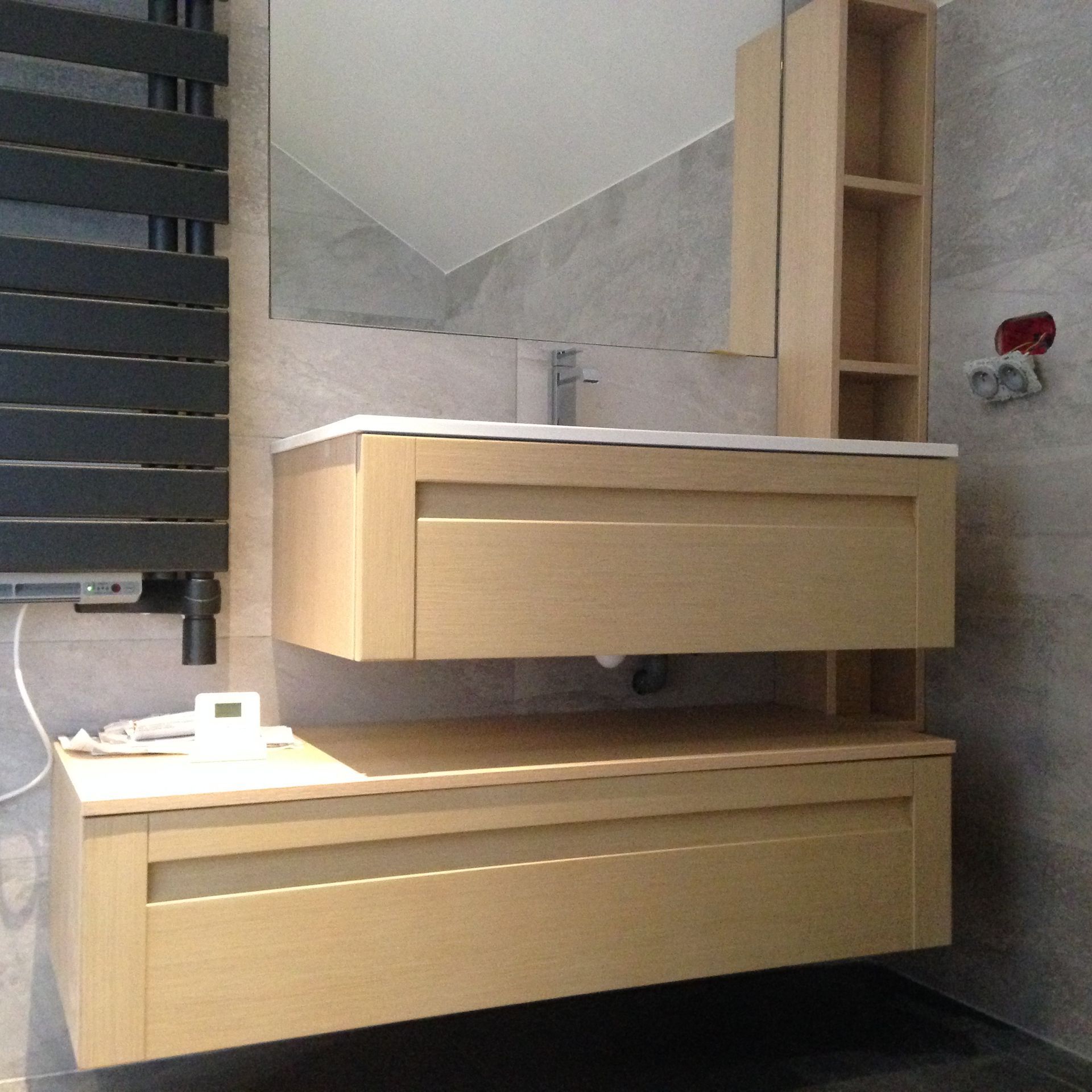 Un meuble lavabo moderne avec deux tiroirs suspendus en bois clair, un lavabo rectangulaire, un miroir et des étagères ouvertes.