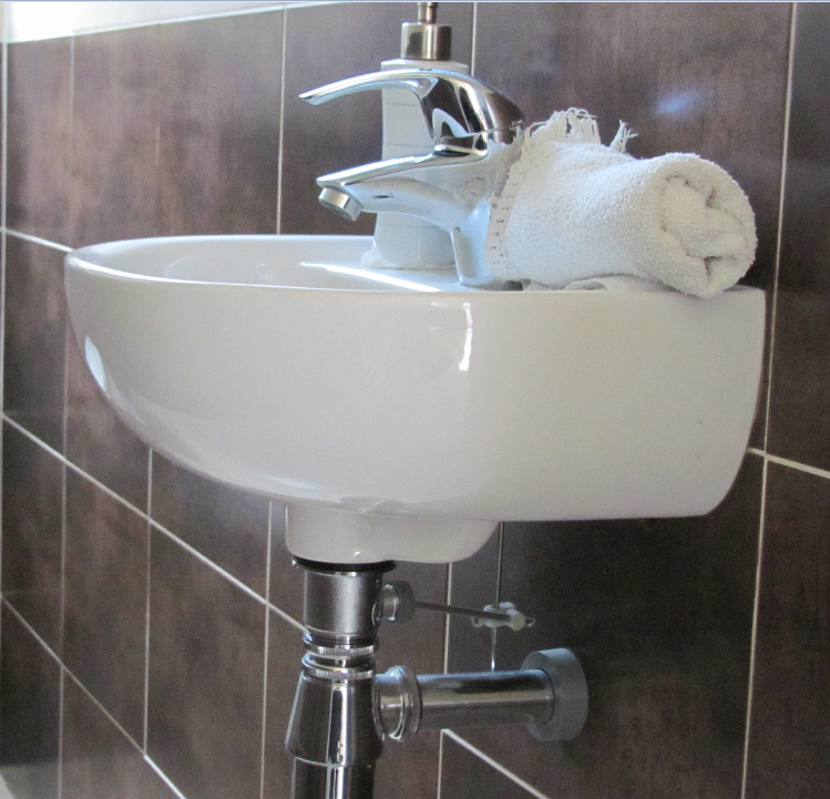 Un lavabo blanc fixé au mur carrelé marron, avec un robinet chromé et une serviette blanche posée sur le lavabo.