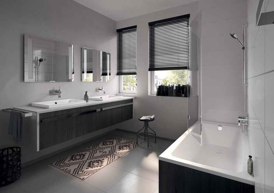 Une salle de bains moderne comprenant une double vasque, des armoires en bois foncé, deux miroirs, un tapis à motifs et une baignoire blanche.