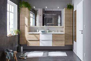 Une salle de bains moderne avec un meuble lavabo en bois clair et blanc, un grand miroir, des armoires murales et des plantes en pot dans une pièce aux tons neutres.