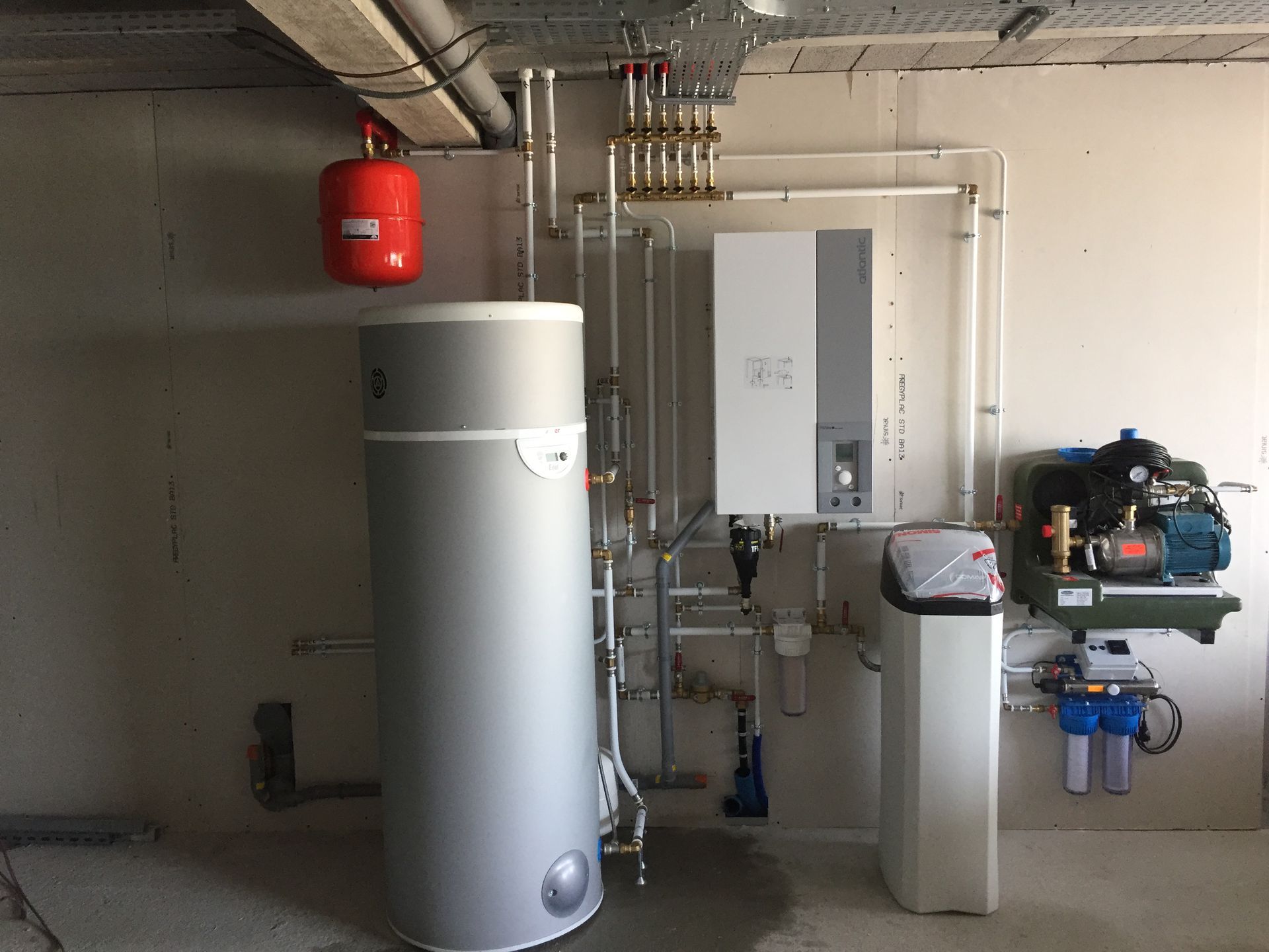 Un système de chauffage résidentiel comprenant un grand réservoir d'eau gris, une chaudière murale blanche et des unités de filtration.