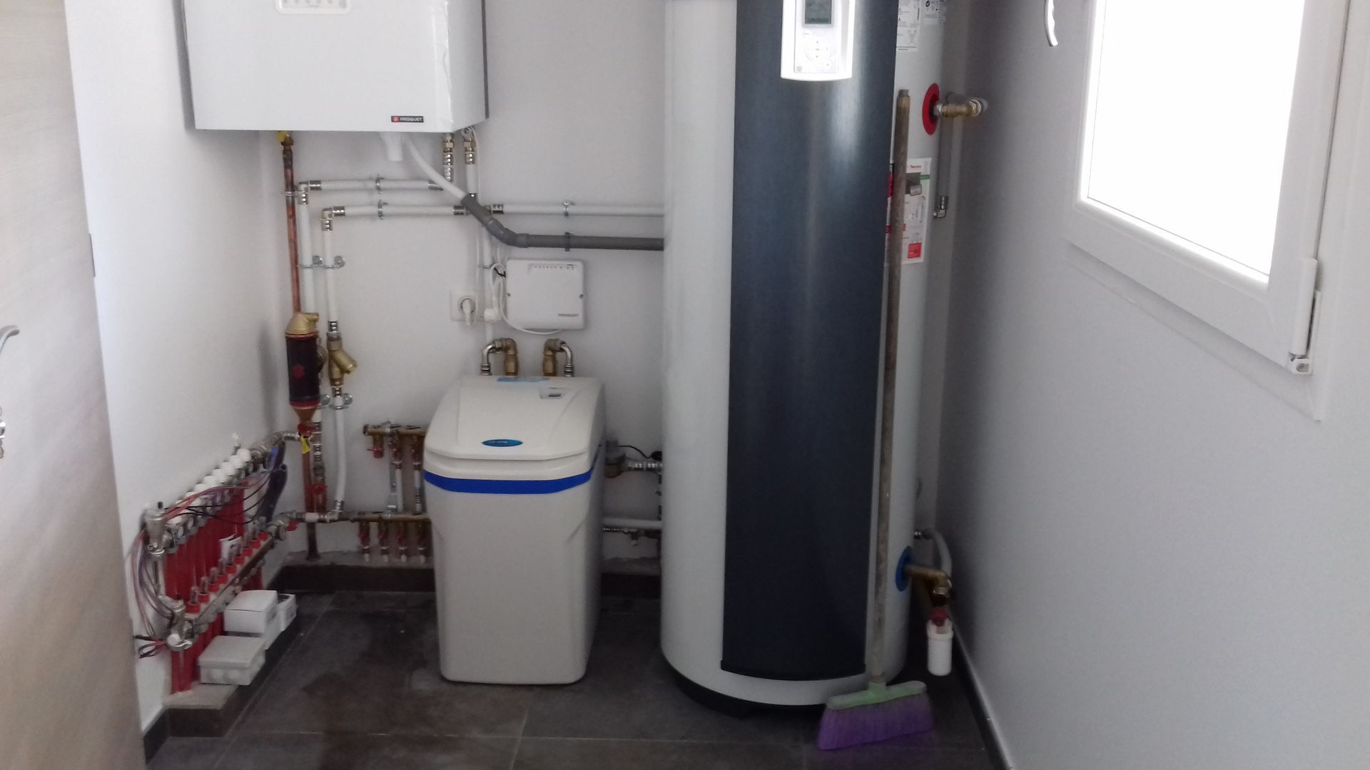 Buanderie avec une chaudière murale, un grand réservoir d'eau chaude blanc et un adoucisseur d'eau compact au sol.