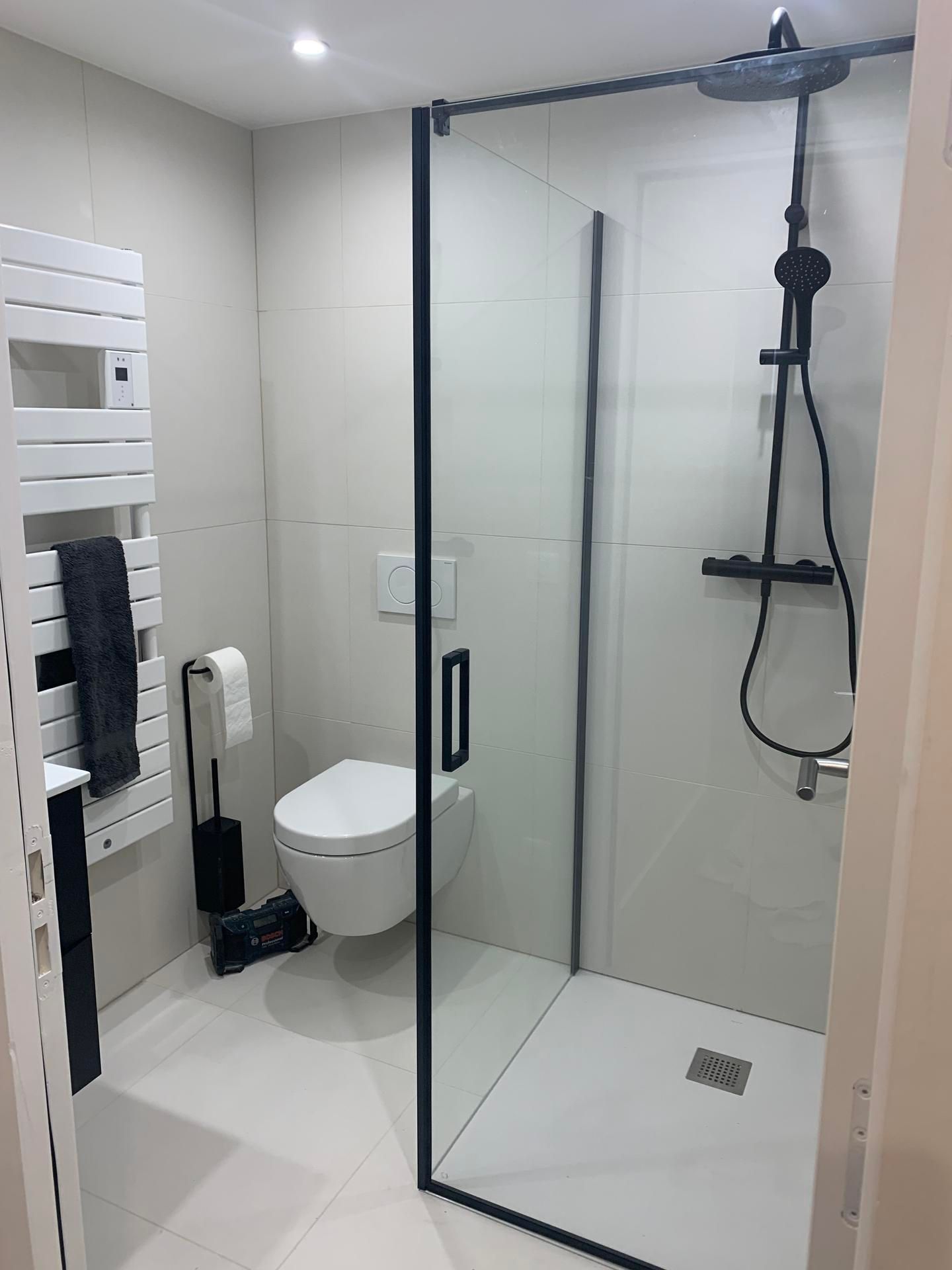 Salle de bains moderne avec douche à l'italienne, toilettes suspendues et sèche-serviettes blanc sur un sol carrelé clair.