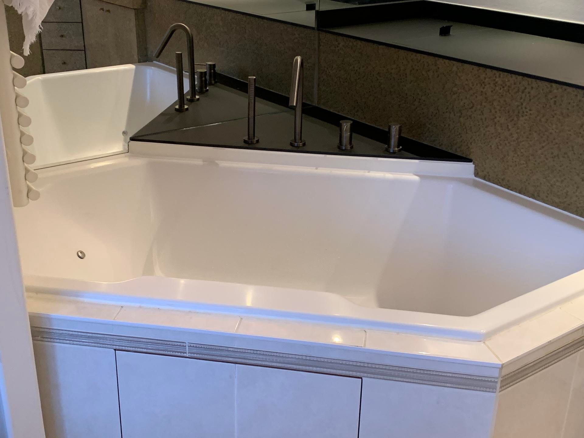 Une baignoire d'angle blanche avec un rebord de comptoir noir, des robinets et des accessoires de plomberie chromés.