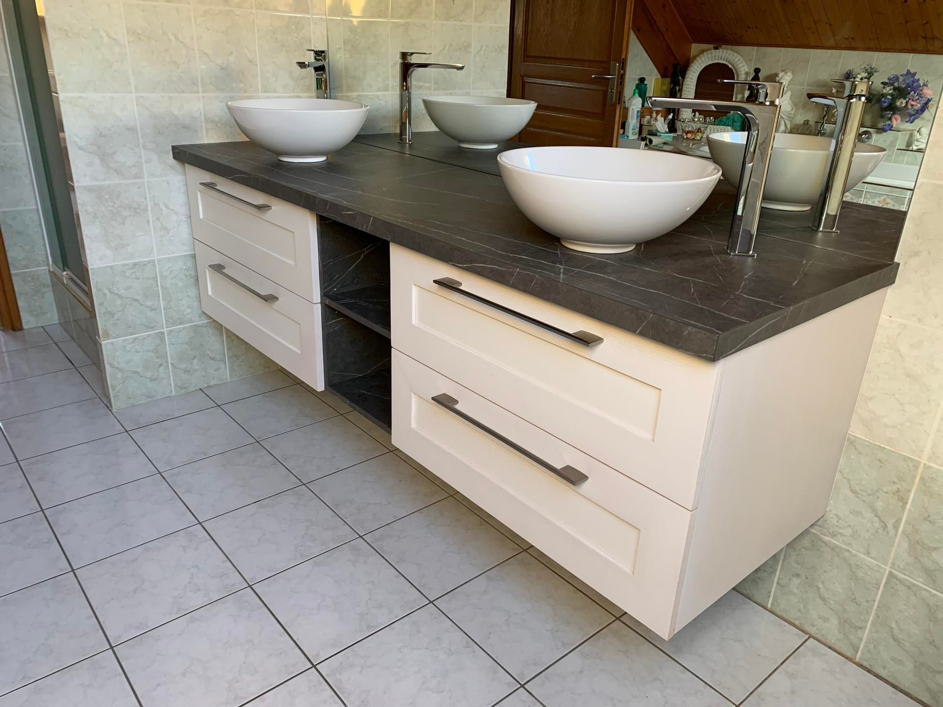 Un meuble lavabo moderne avec deux vasques blanches, des robinets argentés élégants et des tiroirs couleur crème sur un comptoir foncé.