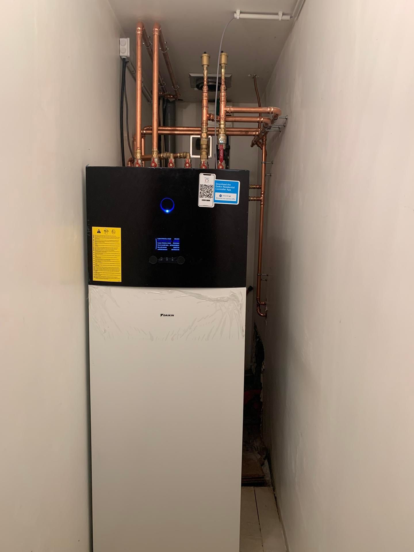 Un chauffe-eau thermodynamique Daikin est installé dans une niche étroite, des tuyaux de plomberie en cuivre partant de son sommet.