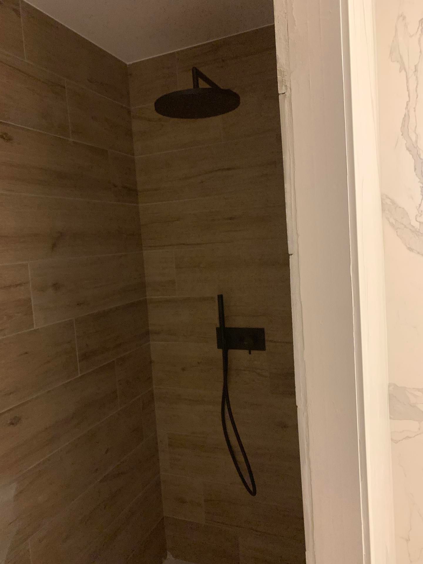 Cabine de douche moderne avec murs carrelés imitation bois, équipée d'une pomme de douche effet pluie noire et d'une douchette.