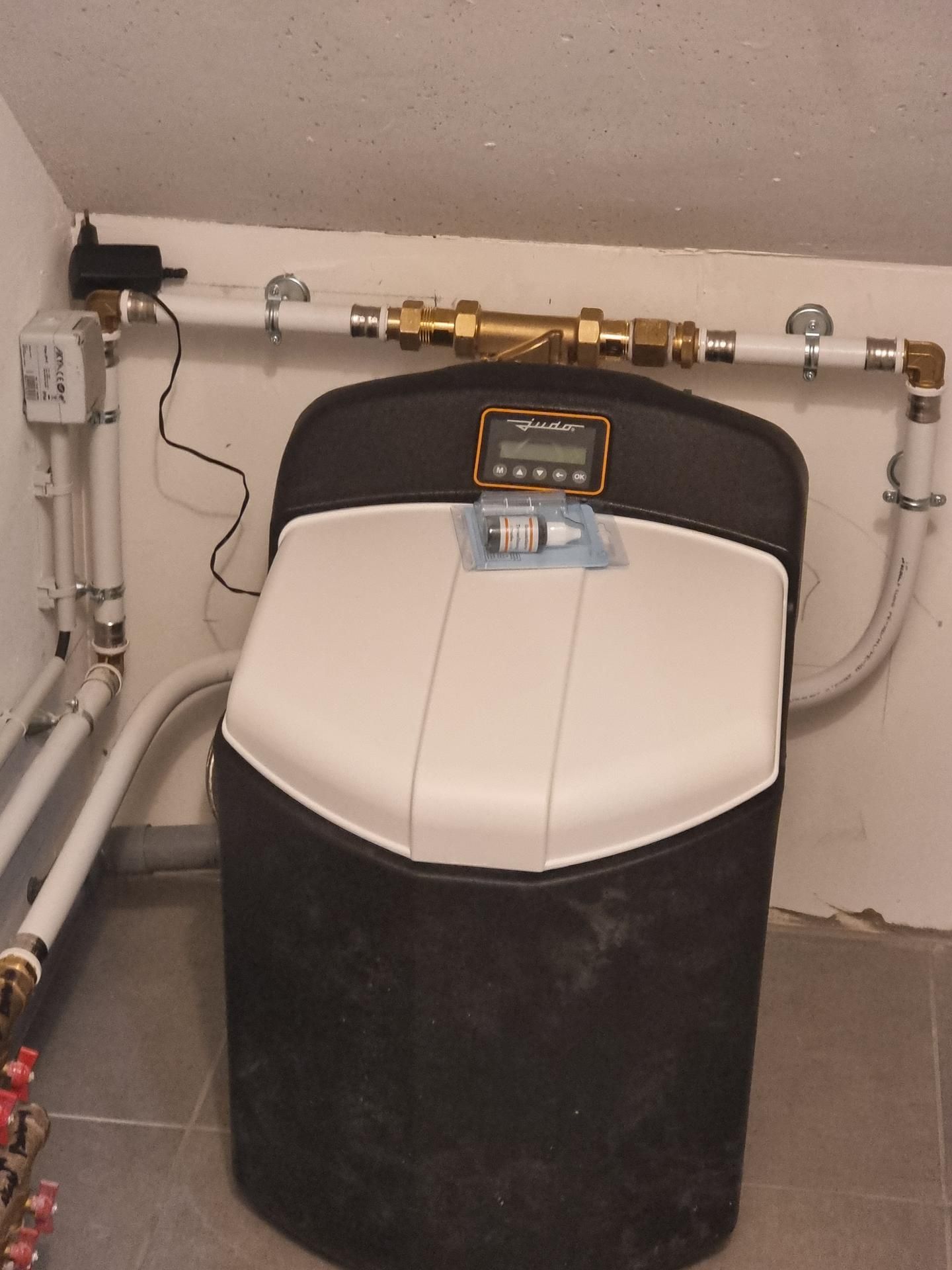 Un adoucisseur d'eau dans un coin, avec des tuyaux blancs, une vanne de dérivation en laiton, un panneau de commande numérique et un kit d'analyse d'eau.