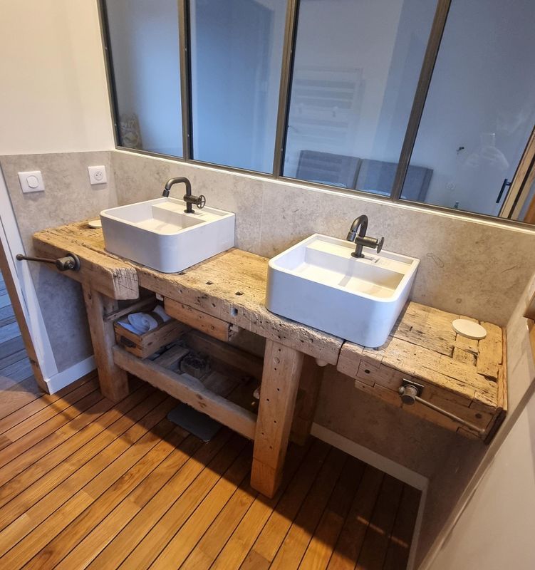 Double vasque avec lavabos carrés blancs sur un établi rustique en bois, avec une cloison en verre dans une salle de bains moderne.