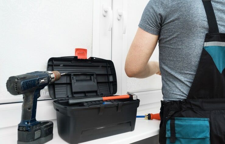 Um homem está trabalhando em uma janela com uma furadeira e uma caixa de ferramentas.