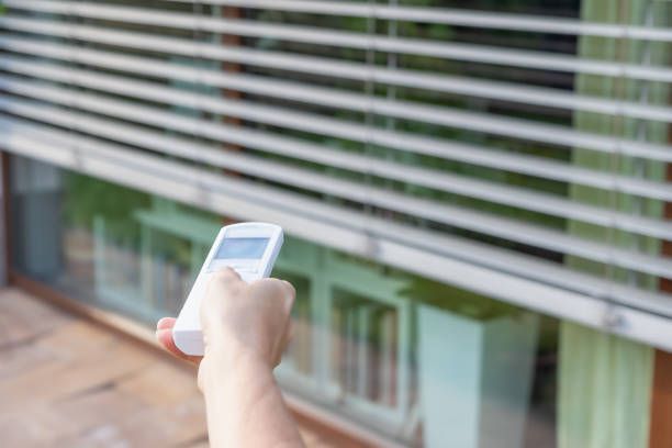 Uma pessoa está usando um controle remoto para abrir uma persiana.