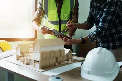Dos trabajadores de la construcción miran una casa modelo sobre una mesa.