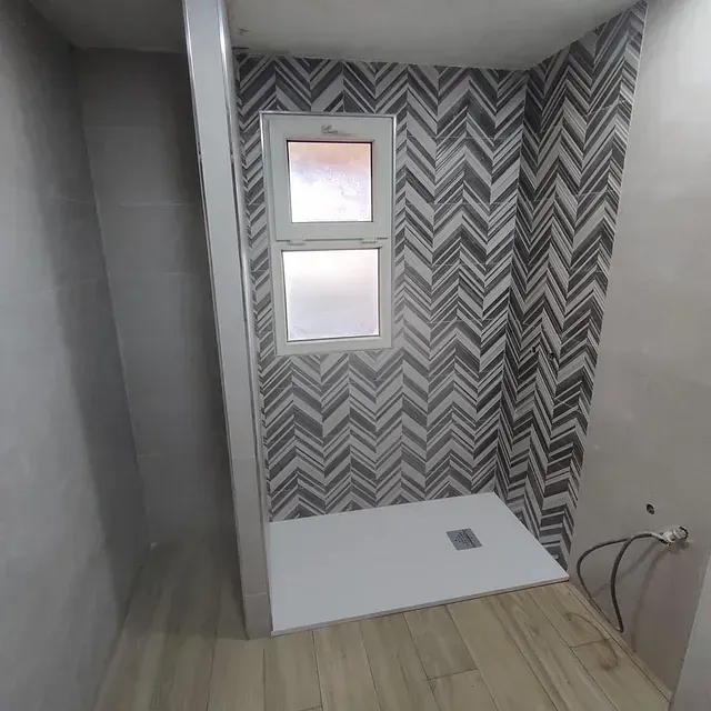 Un baño con ducha y una ventana con un patrón de chevrones en la pared.