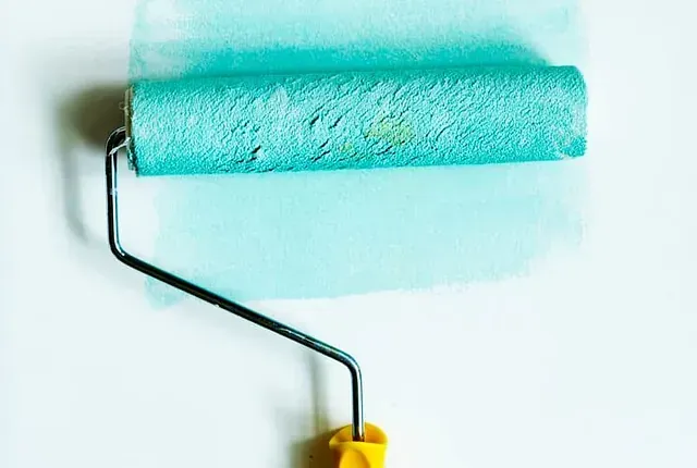 Un rodillo de pintura azul está sobre una pared blanca.