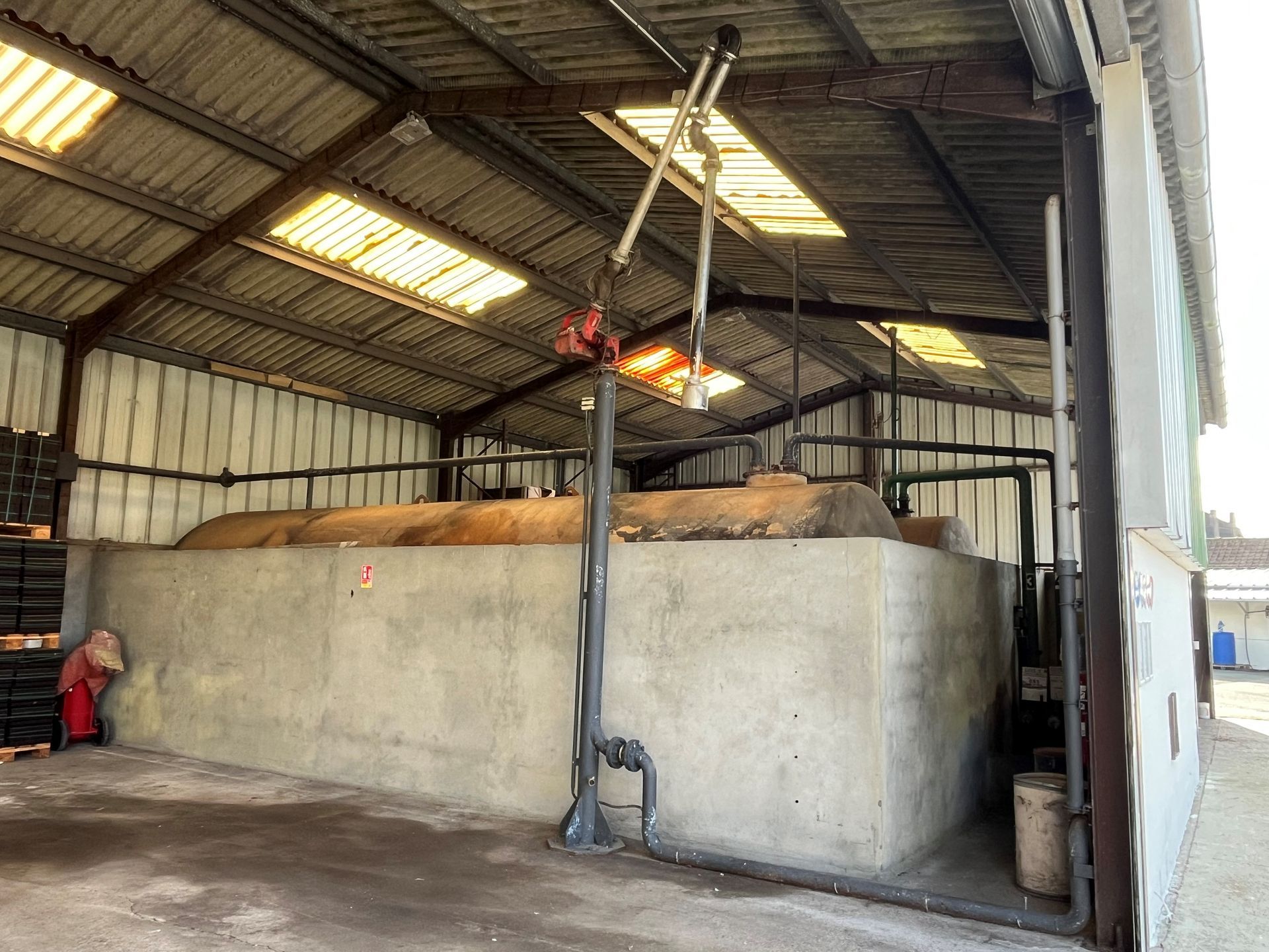 Un grand réservoir de stockage de carburant horizontal se trouve à l'intérieur d'un entrepôt, avec un grand support de pompe de distribution devant lui.