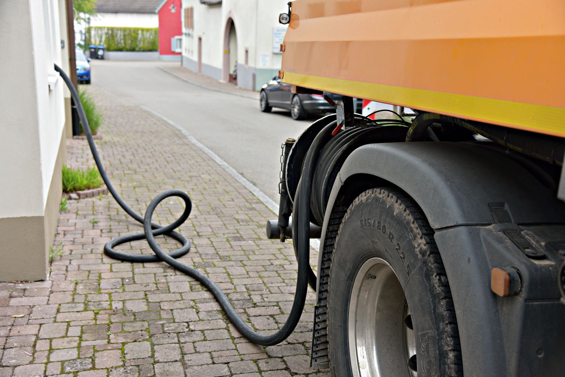 Un tuyau noir relie le mur d'un bâtiment au côté d'un camion de service orange stationné sur une rue pavée.