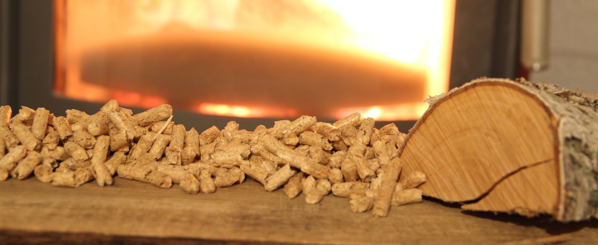 Des granulés de bois et une bûche de bouleau sont posés sur une surface devant une cheminée incandescente.