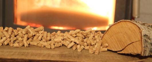 Des granulés de bois et une bûche de bouleau sont posés sur une surface devant une cheminée incandescente.