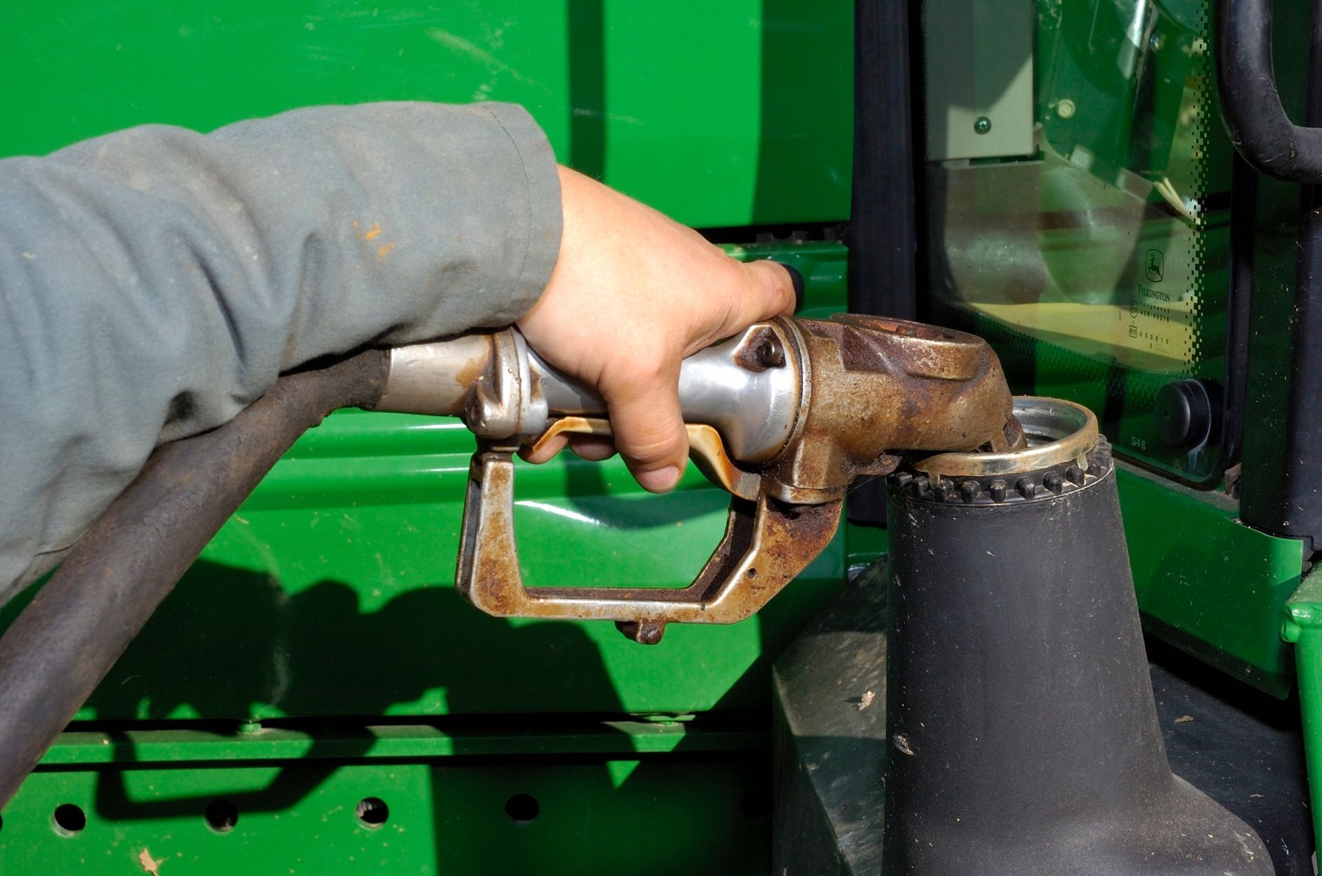 Gros plan sur une main tenant un pistolet à carburant et remplissant un engin vert, probablement un tracteur.